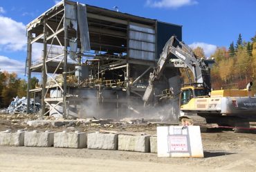 A small steel structure industrial building being demolished by a Démex excavator