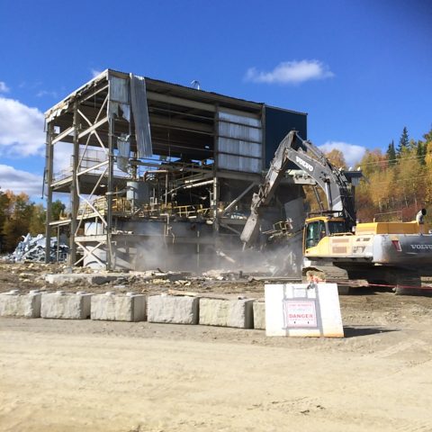 A small steel structure industrial building being demolished by a Démex excavator