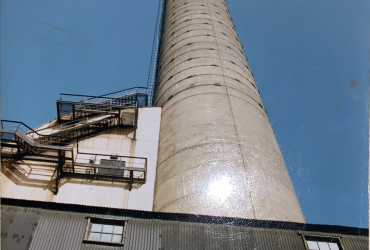 Vue du bas vers le haut de la très haute cheminée de la fonderie Horne, avant le début des travaux, avec ciel bleu en arrière fond.