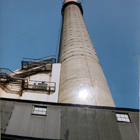 Vue du bas vers le haut de la très haute cheminée de la fonderie Horne, avant le début des travaux, avec ciel bleu en arrière fond.