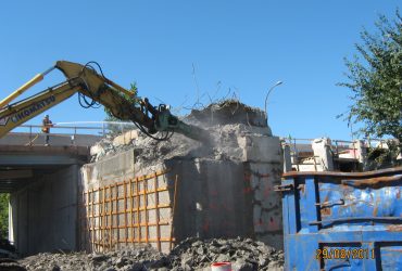 Mat d’une excavatrice Démex équipé d’un marteau hydraulique brisant le béton d’une structure porteuse du pont.