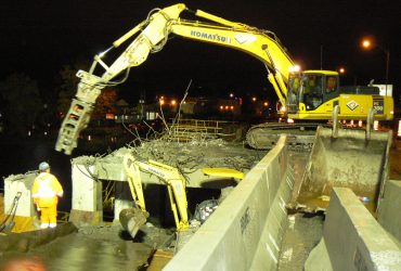 Two Démex excavators and an employee on the bridge at night with artificial lighting