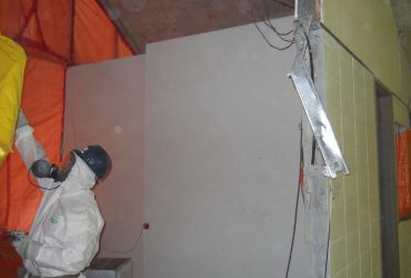 Un employé portant des équipement de protection individuelle et retirant l'amiante à l'intérieur d'un auditorium.