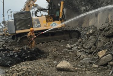 Démex PC 800 excavator at work with an employee spraying water to control dust emissions