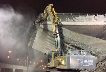 A Démex excavator equiped with a hydraulic hammer demolishing elements of the bridge concrete structure at night with artificial lighting