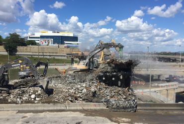 Five Démex excavators demolishing the bridge, crushing concrete and piling concrete on the ground