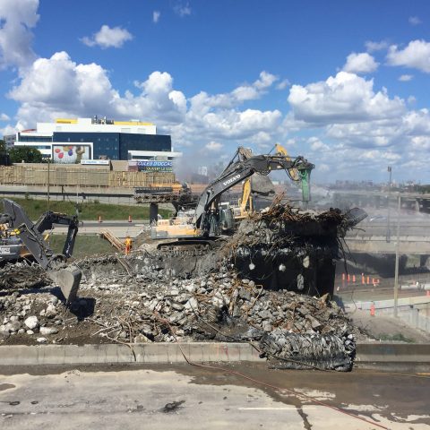 Five Démex excavators demolishing the bridge, crushing concrete and piling concrete on the ground