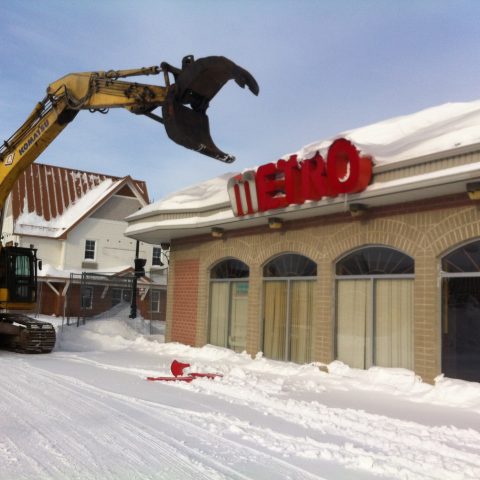 Une excavatrice démolissant la façade d'un magasin Métro