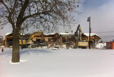 Distant view of two Démex excavators demolishing buildings during the winter