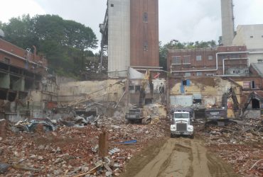 Three Démex excavators picking up demolition debris and loading a truck