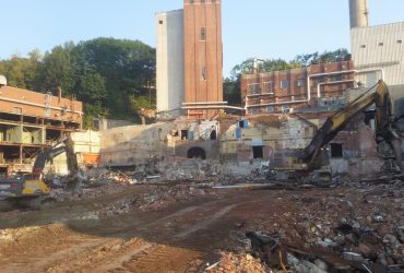 Two Démex excavators piling debris on a section of the site where buildings have already been removed