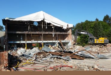 Une excavatrice Démex travaillant sur un bâtiment industriel de 3 étages dont la façade est grande ouverte.