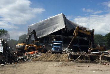 Deux excavatrices, une chargeuse sur pneus et un camion près d'un bâtiment partiellement démoli, le mur avant totalement enlevé.