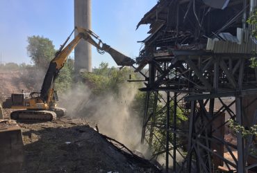 A Démex excavator pulling off elements of the metal structure of a building using a powerful shear