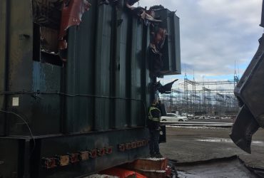 Vue d'un transformateur à démanteler avec la sous-station électrique en arrière fond.