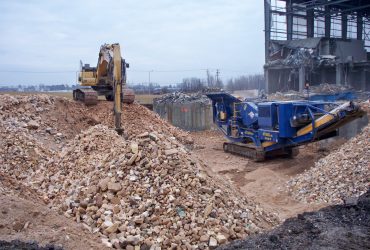 An excavator piling concrete blocks next to a crusher at work