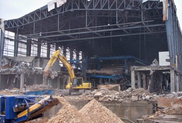 An excavator demolishing elements of the glass production building and a crusher sizing down concrete
