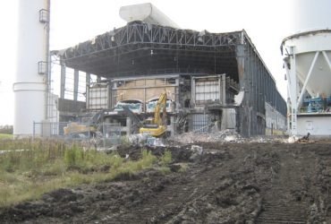 Two excavators working on a building with the front and a side wall wide open