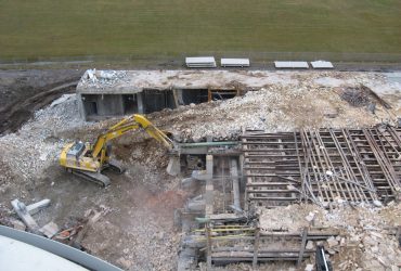 Vue aérienne d'une excavatrice Démex en train de démolir une partie d'un bâtiment en béton.