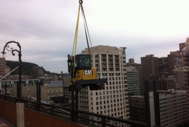 Picture of a small excavator being hoist to the top of the building