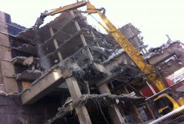 Picture of a long reach excavator equiped with a shear eating away part of the building
