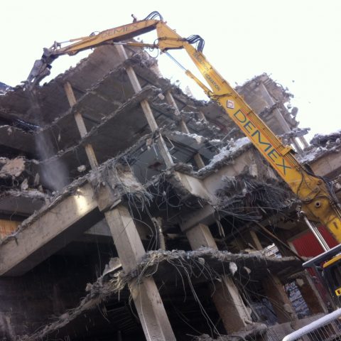 Picture of a long reach excavator equiped with a shear eating away part of the building