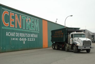 Camion roll-off Démex-Centrem devant le centre de recyclage avec inscription du numéro de téléphone.