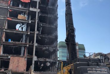 Vue d'une excavatrice Démex à longue portée s'attaquant à la partie supérieur d'une des ailes de l'hôpital.