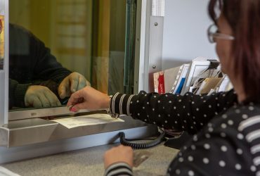 Vue de l'intérieur vers l'extérieur de la préposée à la réception en train de payer un client qui vient de déposer du métal au centre.