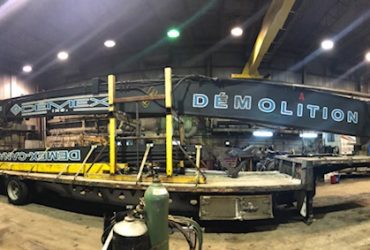 View of a 53 foot section of the PC 800 long reach demolition boom, loaded on a flat bed trailer inside a building