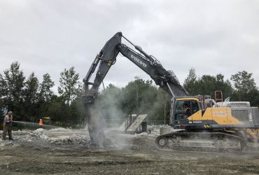 An excavator working and a Démex employee spraying water to control dust emissions