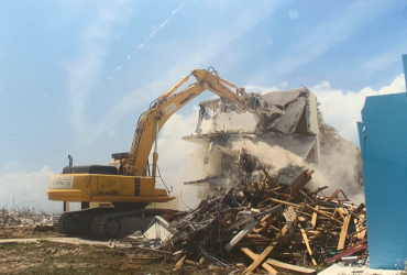 Vue d'une excavatrice Démex munie d'une puissante cisaille en train de démolir un bâtiment en béton.