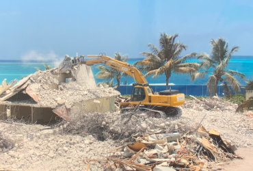 Excavatrice démolissant une structure de béton par temps ensoleillé avec vue sur la mer.