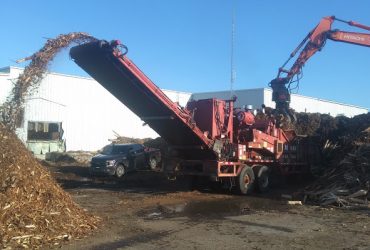 Wood chipper being loaded with a grapple equiped excavator and downsized wood pieces expelled onto a pile