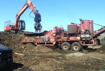 VExcavator equiped with a grapple loading the wood chipper with biomass