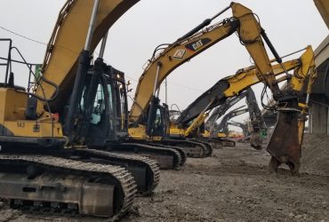 Vue de six excavatrices au repos, alignées devant une section de voie surélevée à démolir, par temps gris.