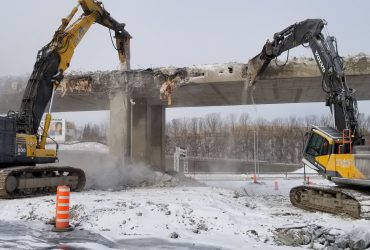 Vue de deux excavatrices broyant le béton d'une rampe d'accès élevée au niveau Angrignon. en hiver par temps ensoleillé.