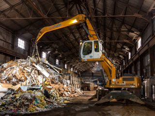 Vue intérieure du secteur de gestion de débris de construction, rénovation et démolition avec une excavatrice de manutention avec grappin en train d'empiler des débris.