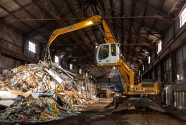 Vue intérieure du secteur de gestion de débris de construction, rénovation et démolition avec une excavatrice de manutention avec grappin en train d'empiler des débris.