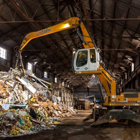 Vue intérieure du secteur de gestion de débris de construction, rénovation et démolition avec une excavatrice de manutention avec grappin en train d'empiler des débris.