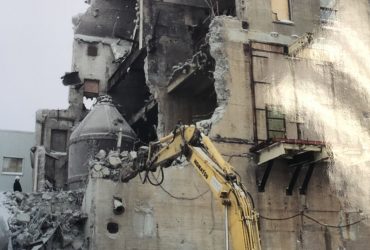 Vue d'une excavatrice Démex en train de gruger un mur extérieur d'un bâtiment en béton.