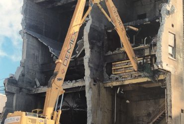 Vue d'une excavatrice en train de démolir un bâtiment en béton à moitié ouvert.