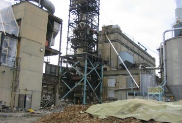 Photographie de la base de la structure métallique de l'ancien atelier de production d'acide avec pile de bois broyé recouverte d'une membrane pour amortir sa chute et minimiser le dommage au sol.