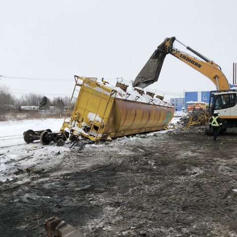 Excavator using a powerful shear tool to cut up a yellow tanker car