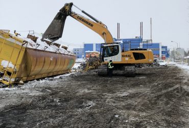 Photo d'un autre wagon de couleur jaune en cours de démantèlement par une excavatrice munie d'une puissante cisaille, par temps gris en hiver.