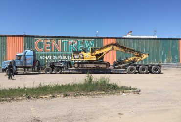 Excavator loaded onto a low deck trailer at Centrem recycling center in Alma