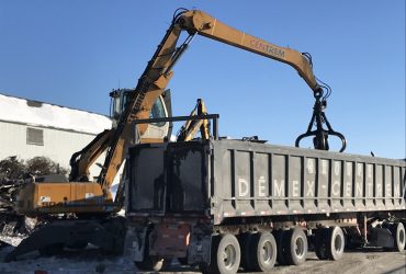 Vue d'une excavatrice de manutention mobile munie d'un grappin en train de charger des métaux dans une benne