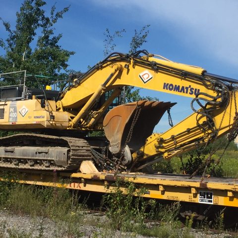 Vue d'une excavatrice PC 400 sur fardier ferroviaire par très beau temps.