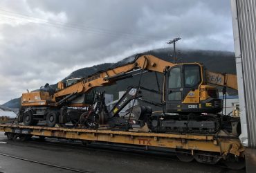 Vue de deux équipements mobiles sur fardier ferroviaire par temps gris.