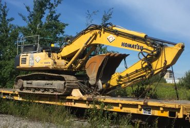 Vue d'une excavatrice PC 400 Démex sur wagon-fardier par beau temps.